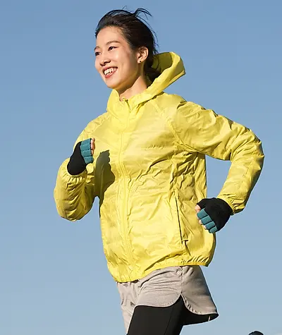 Woman smiling as she runs while wearing a lightweight yellow rain jacket